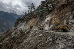Heavy machinery cutting into a steep Himalayan mountainside for road widening, showing environmental impact.